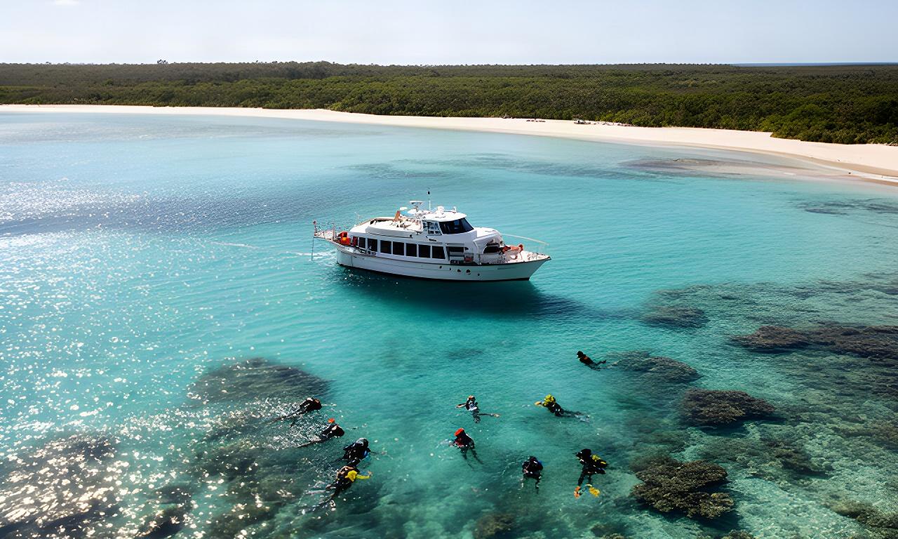 Small expedition cruise vessel beside a sheltered Great Barrier Reef lagoon as snorkellers explore clear water
